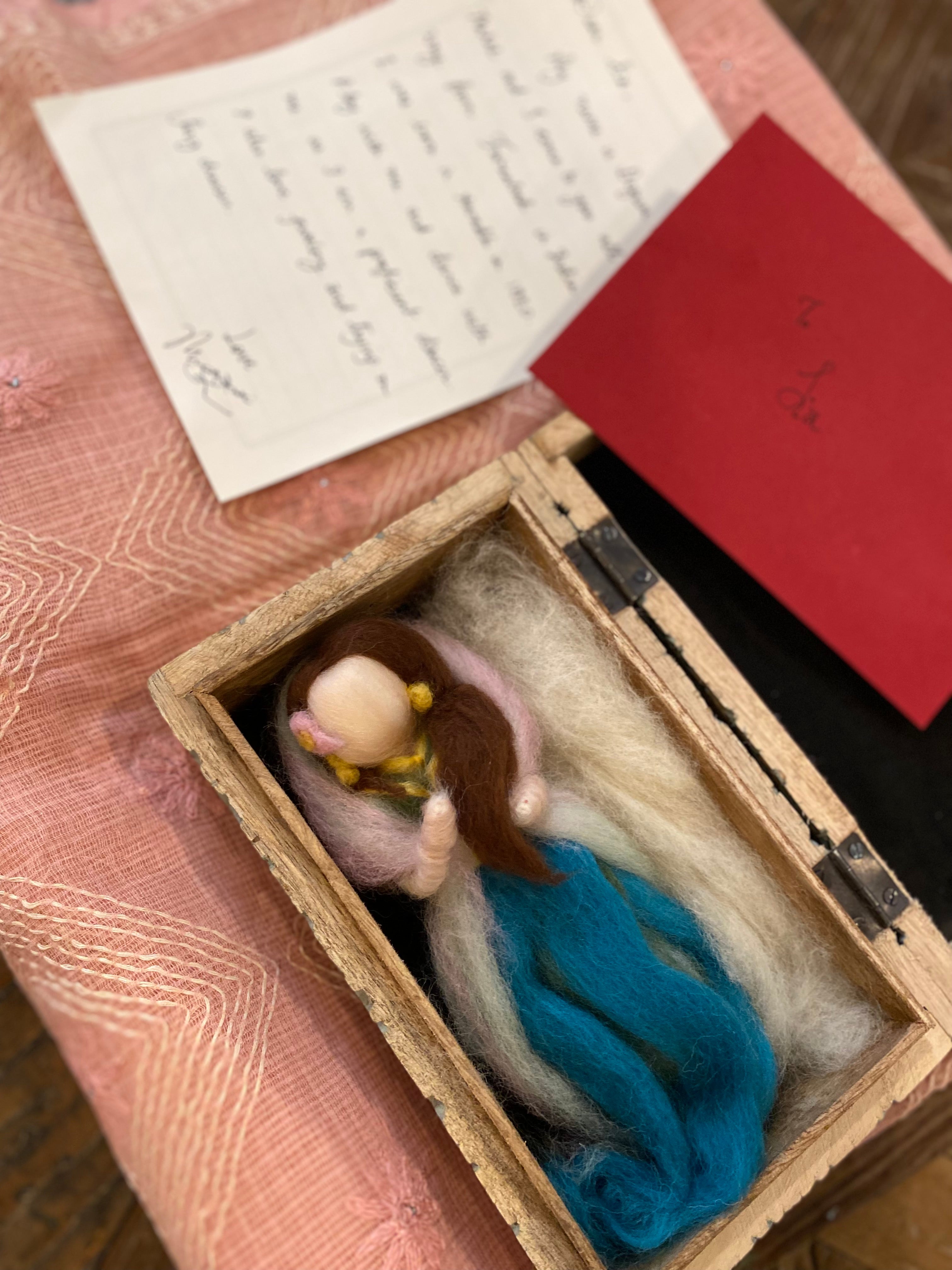 wooden box holding a wool felt fairy depicting a South Asian queen accompanied by letter